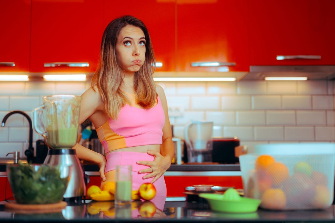 Woman experiencing bloating in her kitchen before exploring natural herbal remedies for digestive wellness.