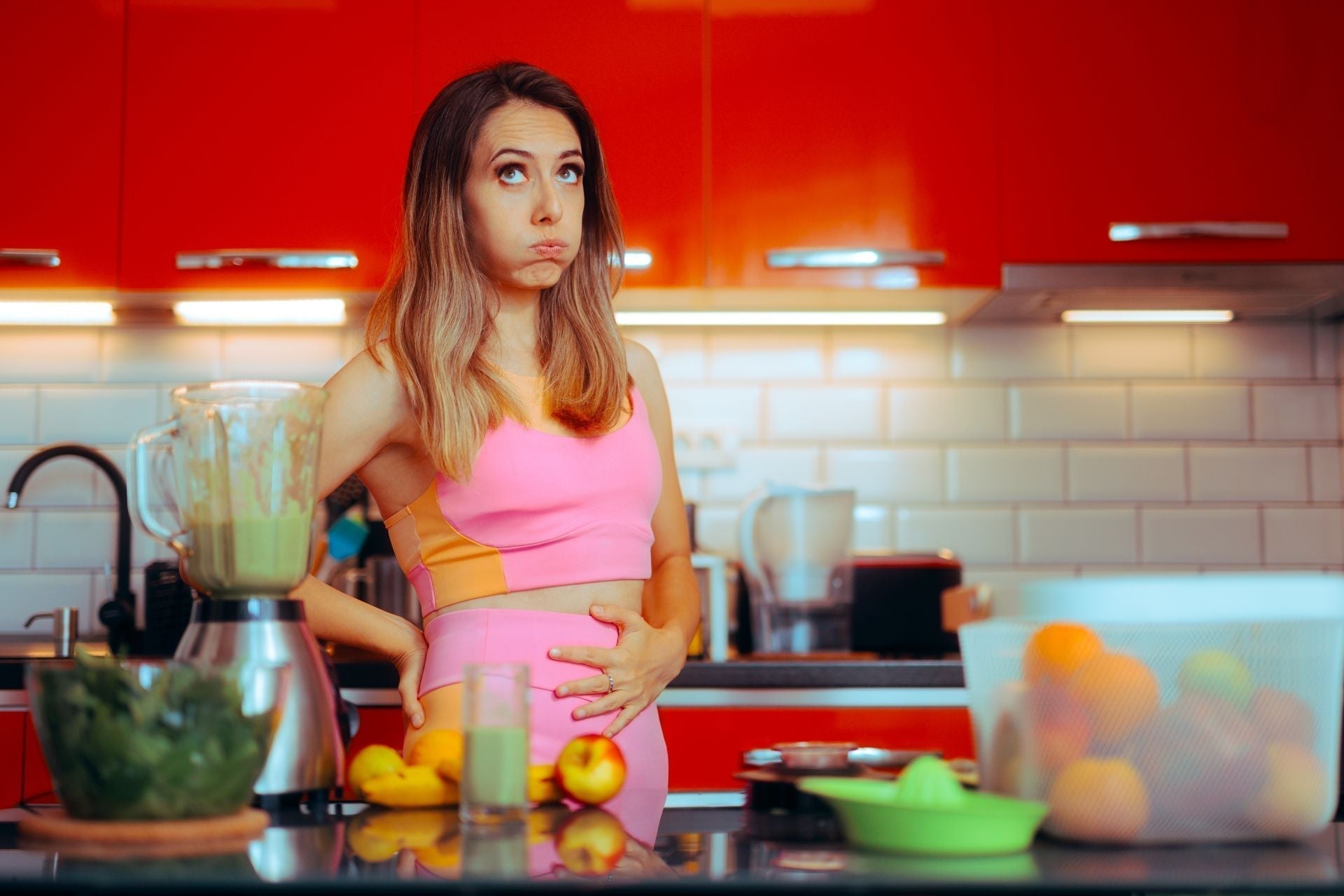 Woman experiencing bloating in her kitchen before exploring natural herbal remedies for digestive wellness.